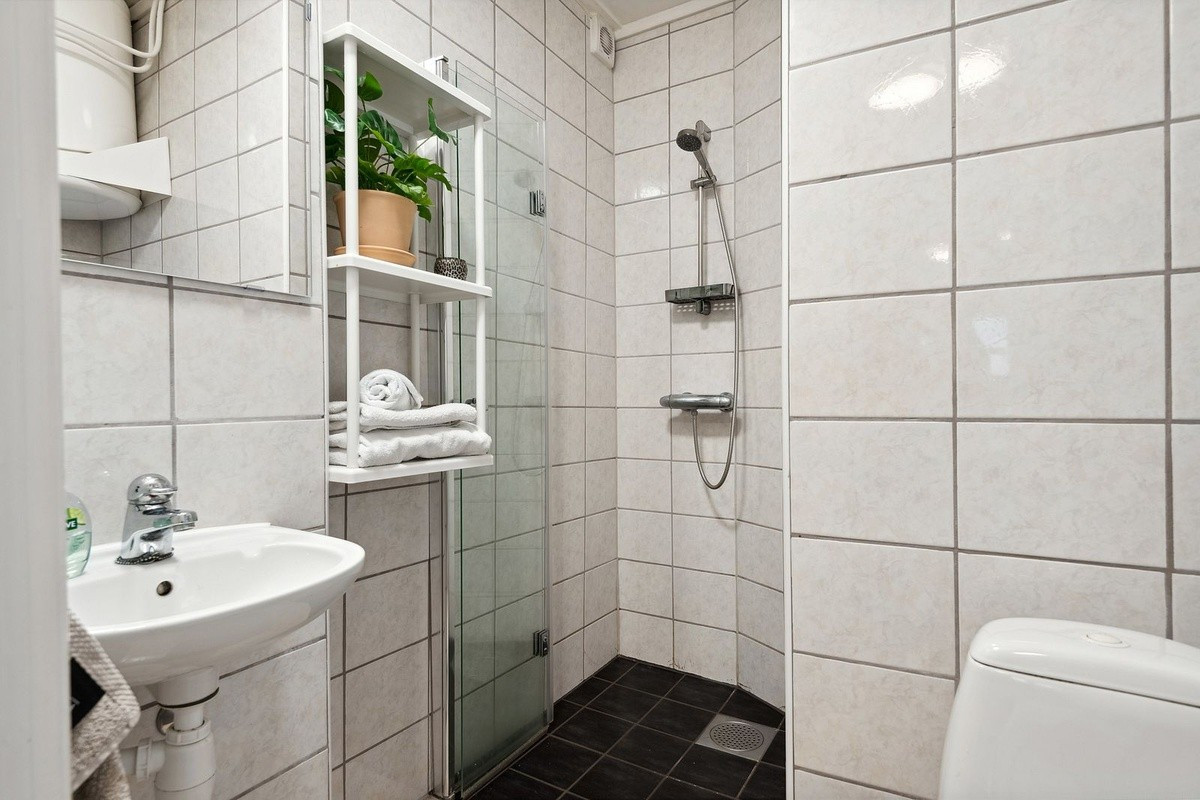 Flislagt bad med toalett, dusjhjørne, vaskemaskin og varmekabler i gulv.