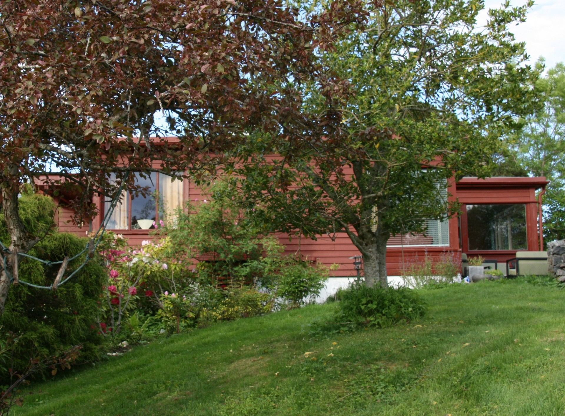 Plassert på en høyde pent i terrenget med romslig hage. Hovedinngang har trapp. Utgang fra hagestue til steinlagt terrasse