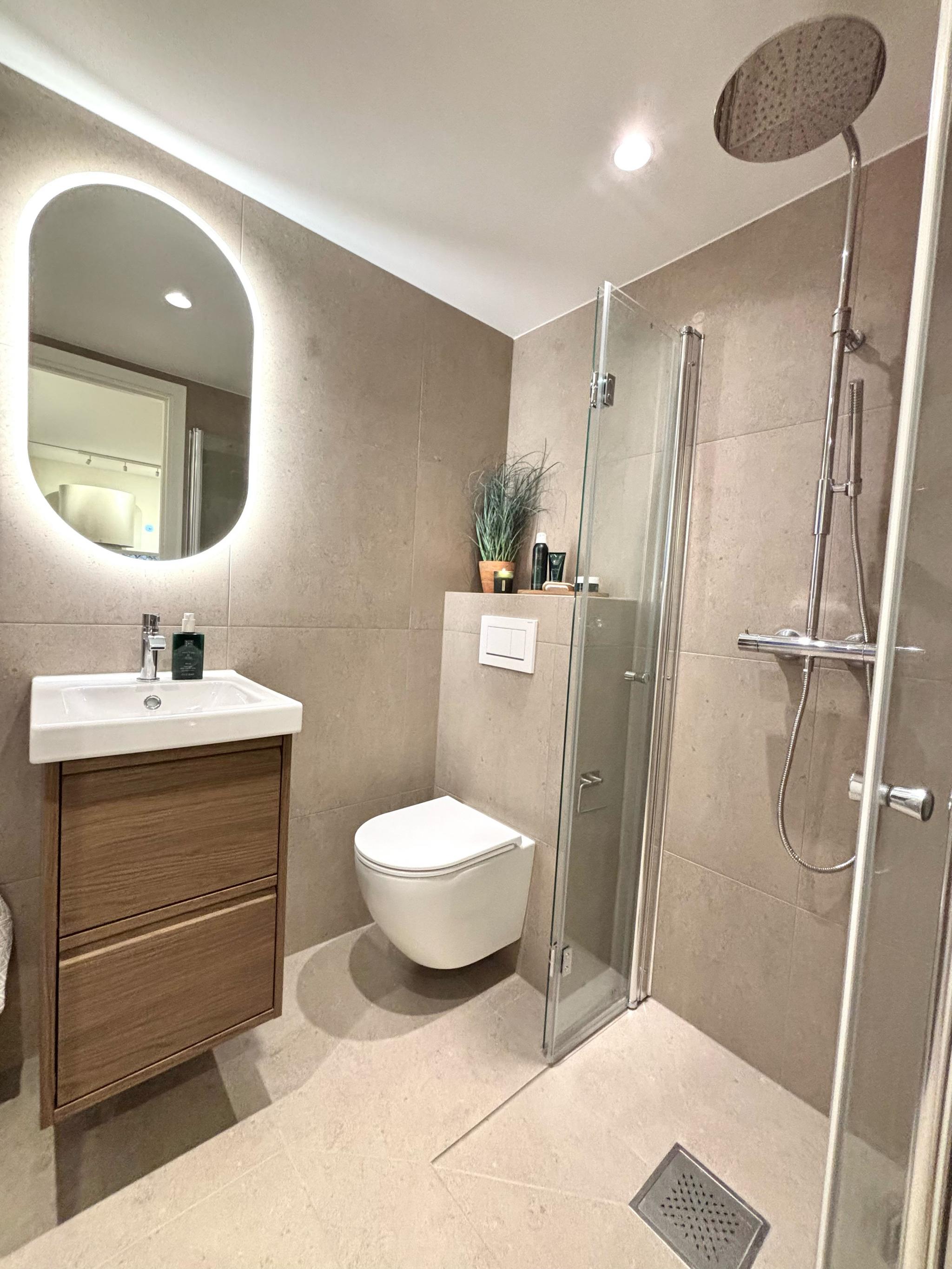 Flislagt bad med spotter i tak og speil med lys. 