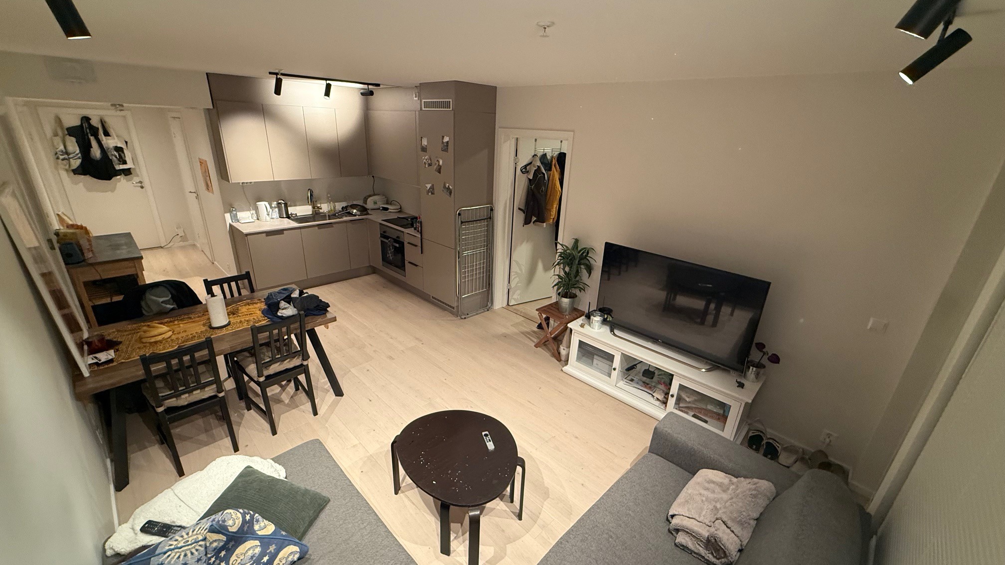 Vidvinkel av kjøkken, stue og sofakrok. Viser også inngang til det minste soverommet og utgang til terrasse på høyre side