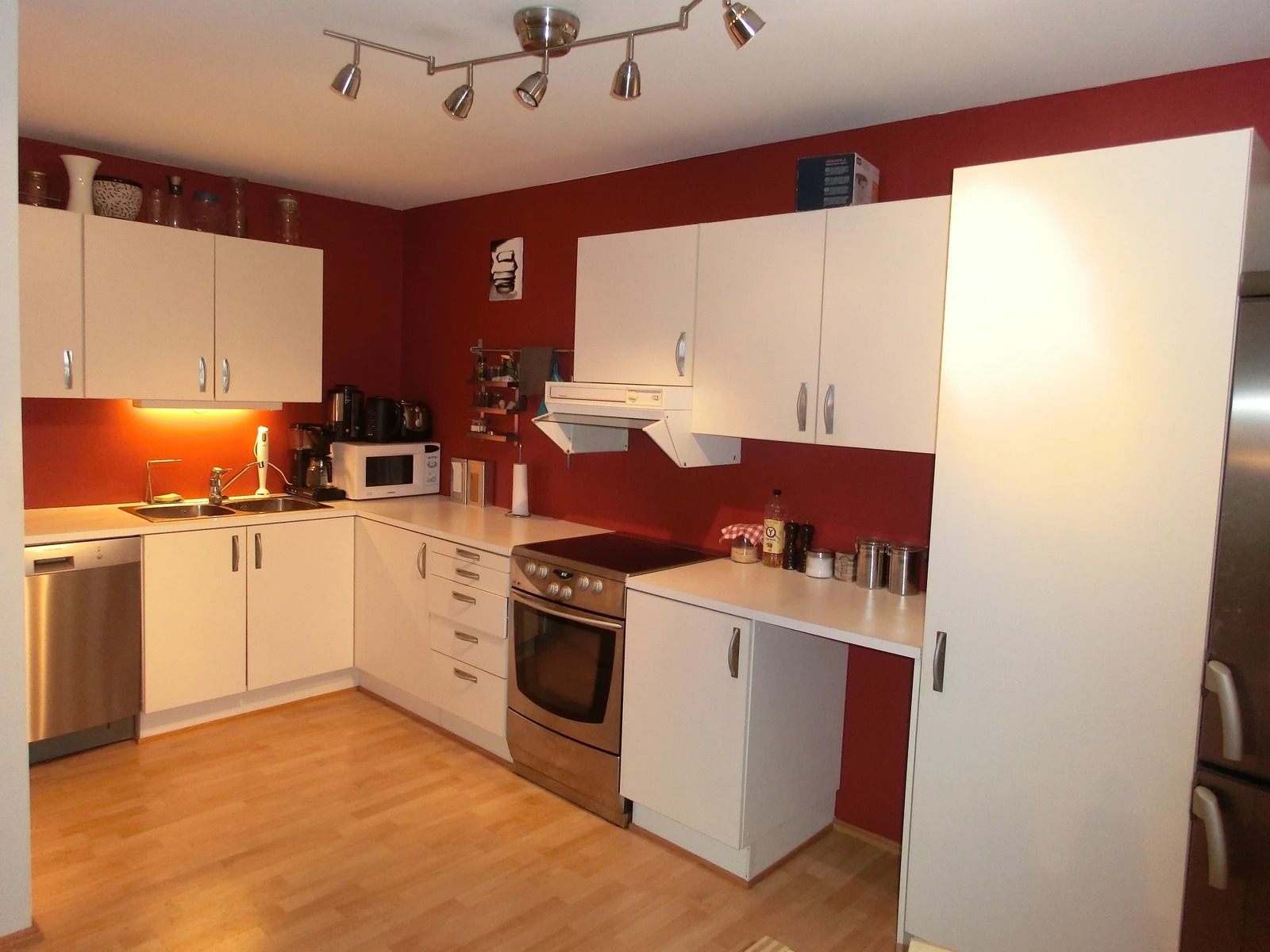 Åpen kjøkkenløsning med komfyr, kjøleskap og oppvaskmaskin. Kjøkkenet er nå malt beige.