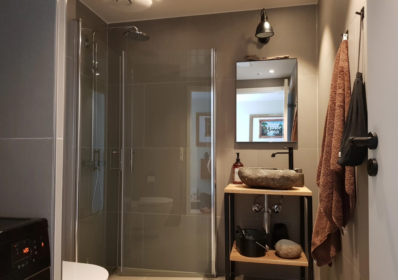 Badet inneholder dusj, vask, et lite veggskap og vaskemaskin.