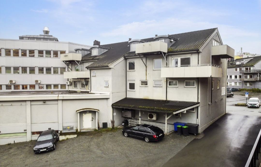 Bygningen til leiligheten fra bakgården. Boden i kjelleren er ned trappen ved siden av den parkerte sorte bilen. For visning gå inn døren til høyre for BMWen i bakgården på bilde og opp til 2. etasje. Leiligheten er til høyre av de 3 leilighetene i 2. etasje. Parkeringsplassen til leiligheten er der BMWen er parkert.