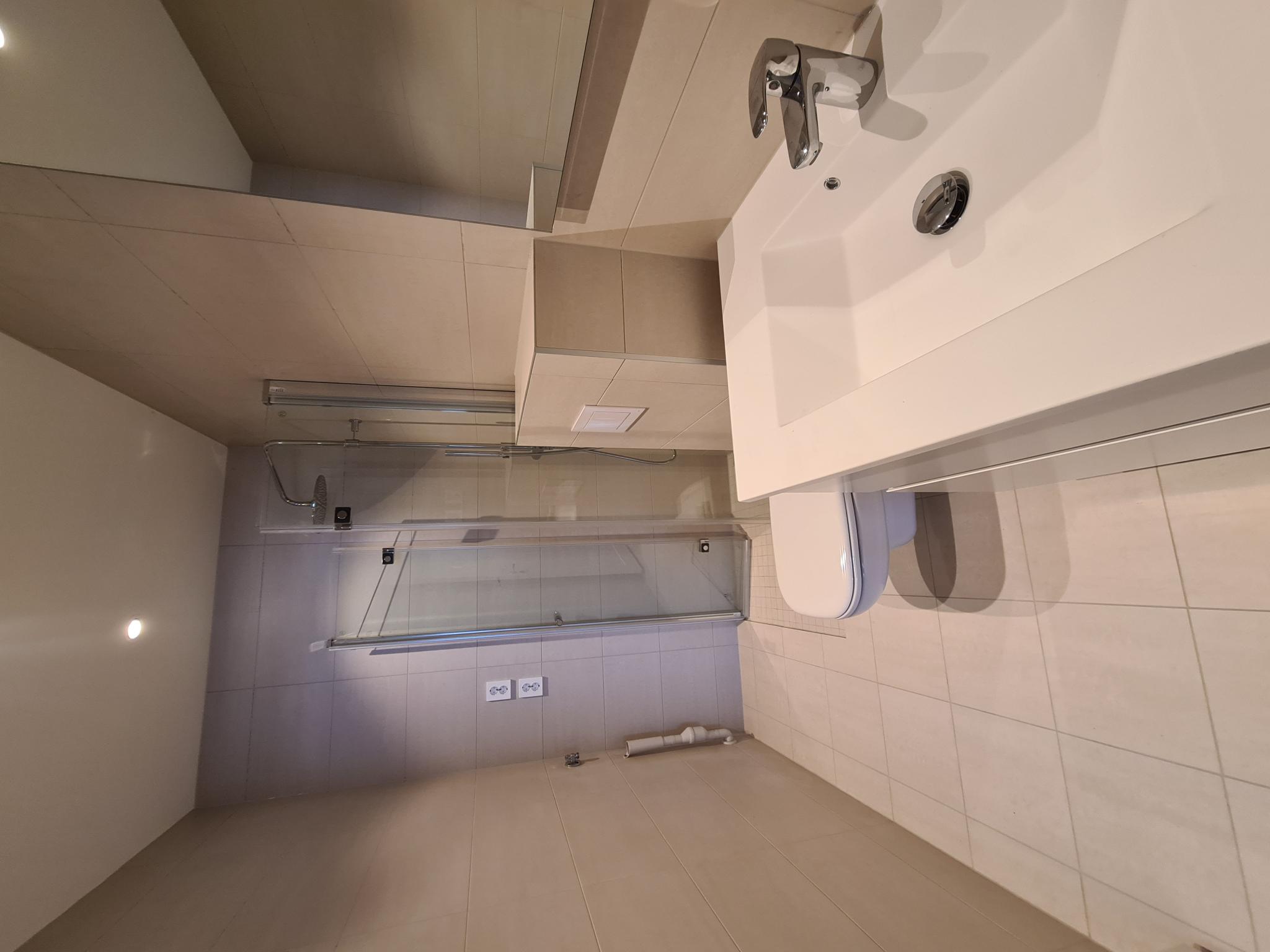 Moderne og lyst bad med vegghengt toalett, servant med skuffeseksjon, vegghengt speil og dusjhjørne med glassdører
