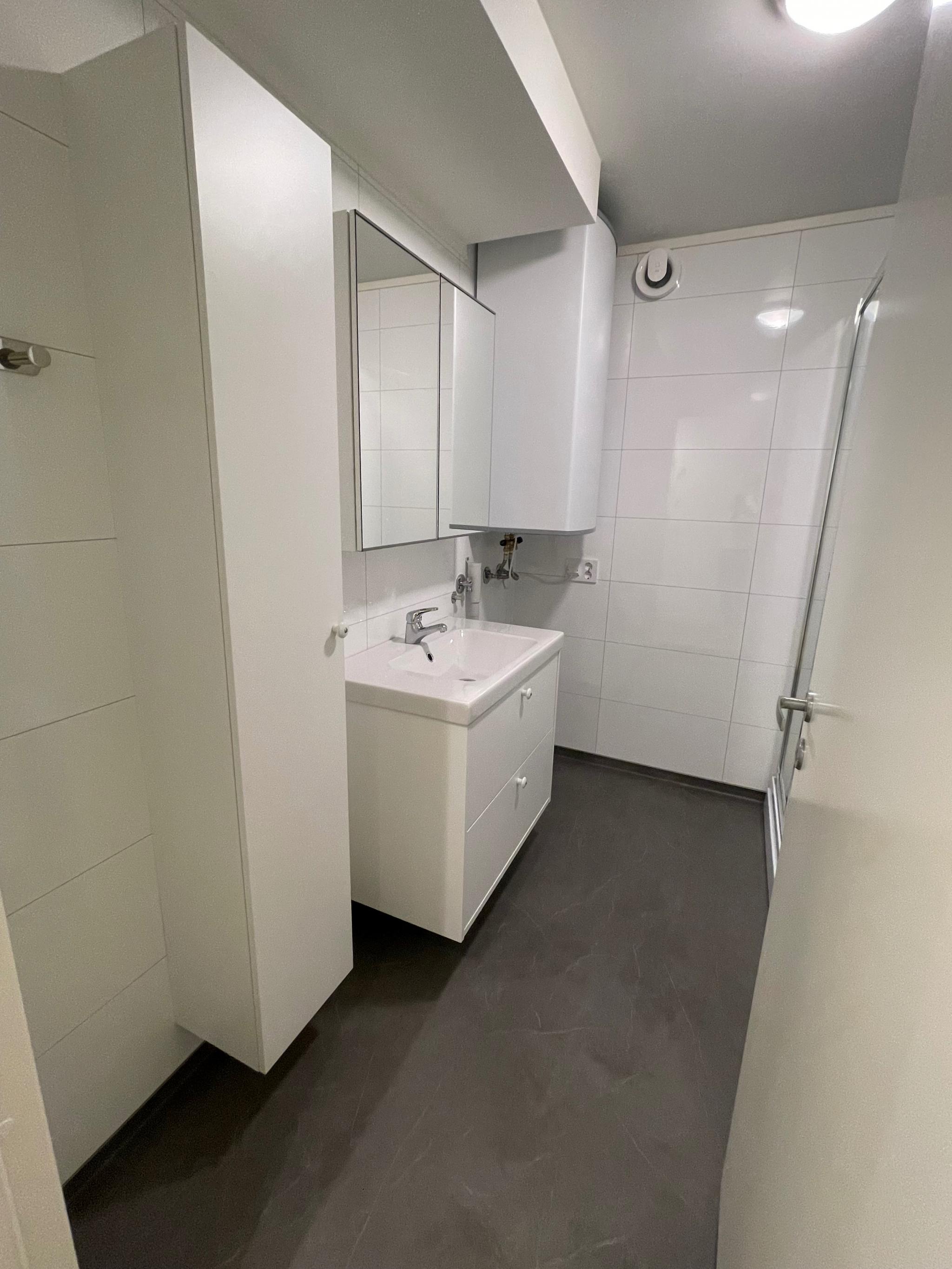 Bad med varmekabler i gulv, plass til vaskemaskin og høyskap for lagring.