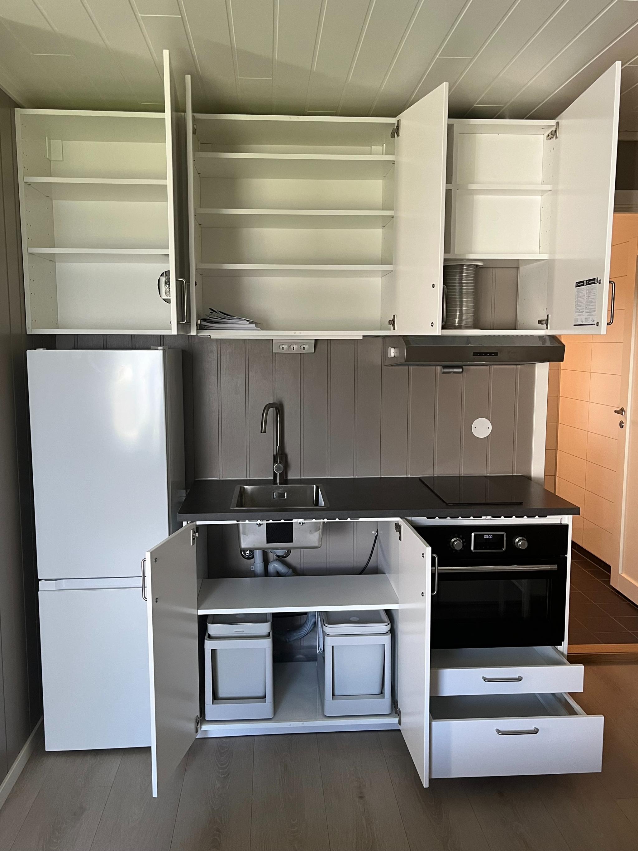 Kjøkken utstyrt med stekeplate, kombinert kjøleskap/frys, stekeovn med mikrofunksjon og ventilator.