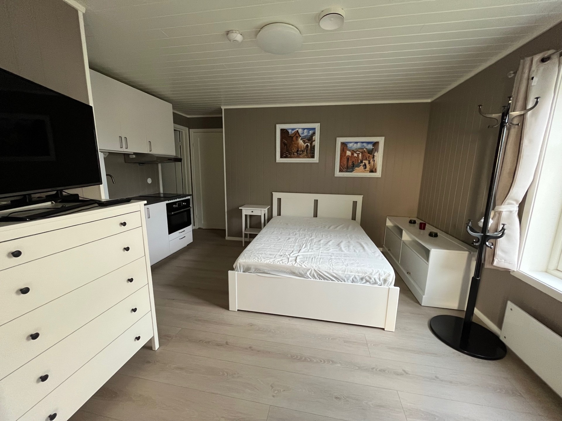 Romslig soverom utstyrt med en 140x200 cm seng, nattbord, kommoder, speil, gardiner, klesstativ, TV-hylle, garderobe og kommoder