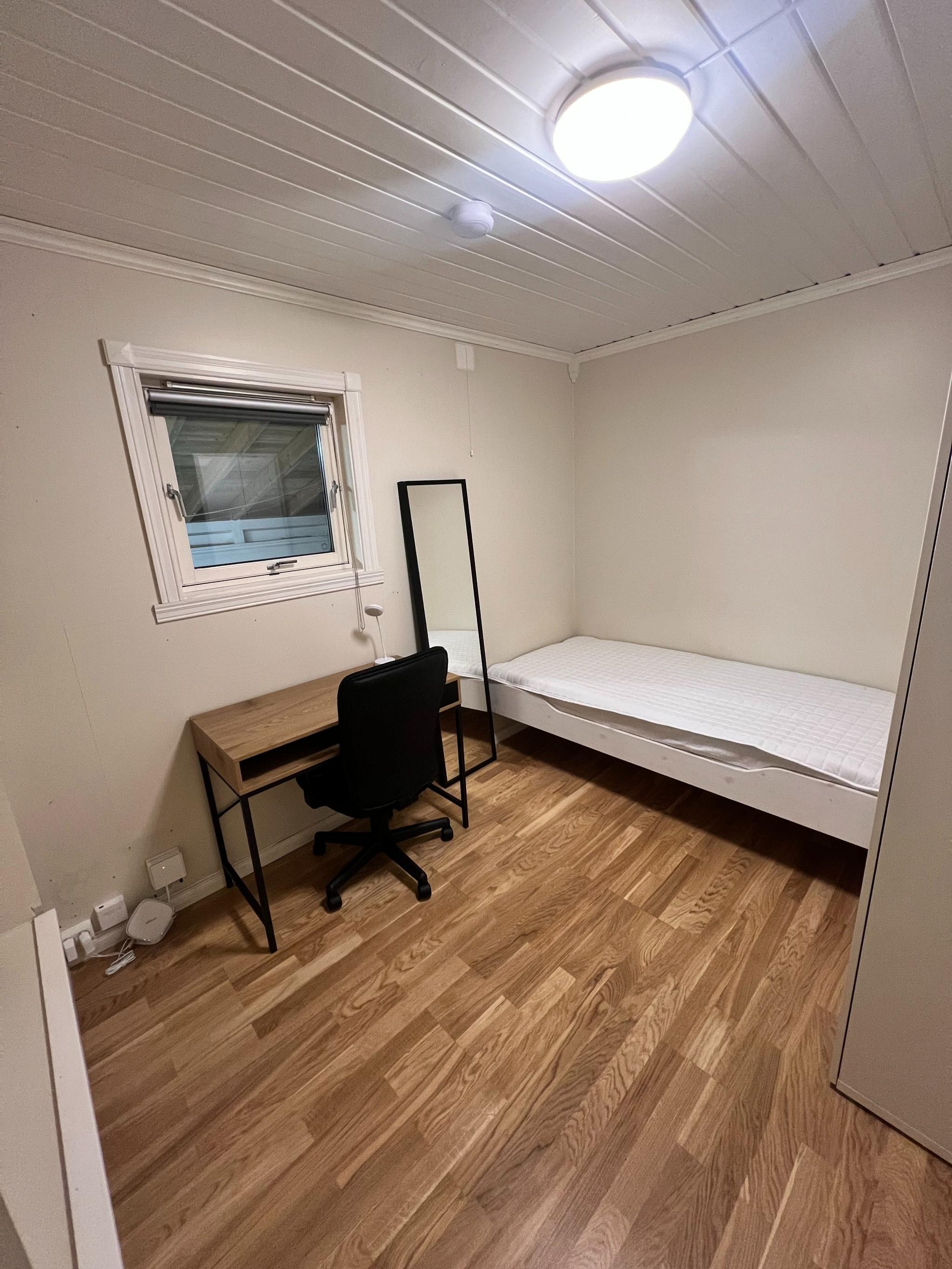 Soverom med seng, speil, garderobeskap, skrivepult, kontorstol og lampe