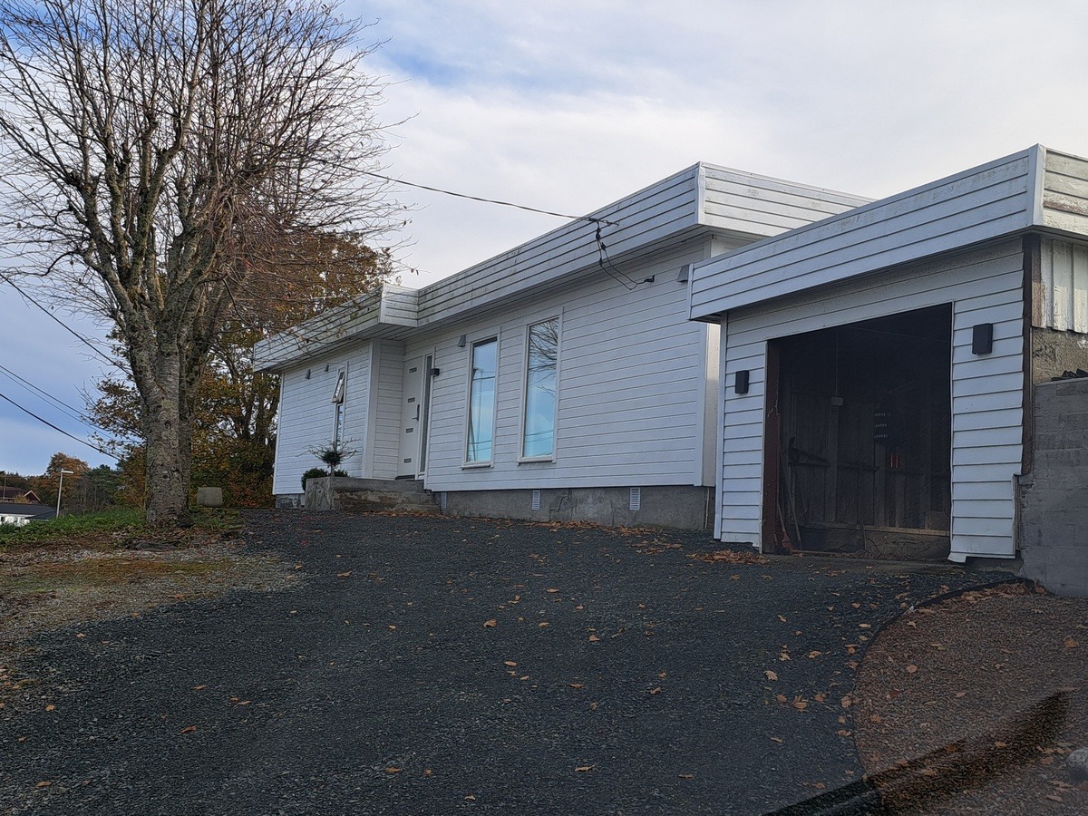 Husfasade. Garasje og stor parkeringsplass.