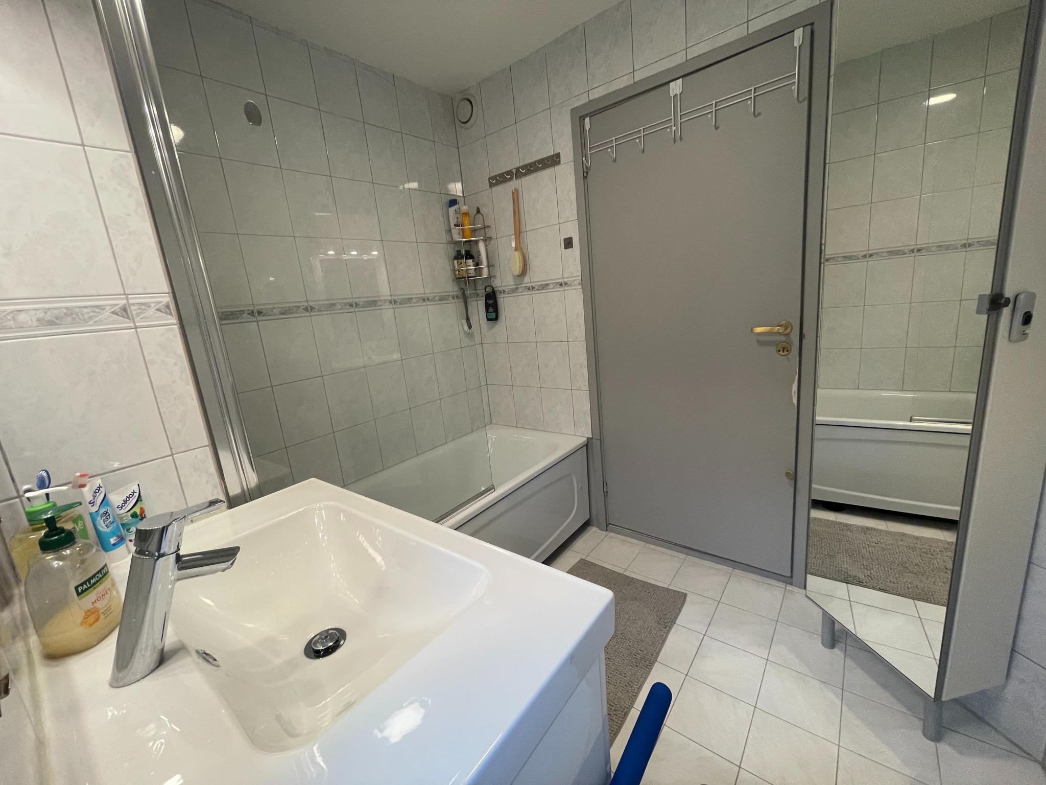 Flislagt bad utstyrt med speil, servant, toalett og badekar med dusj.