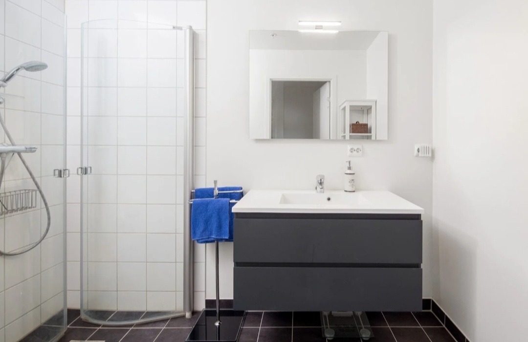 Baderom med romslig baderoms møblement, vegghengt toalett og praktisk dusj med vendbare glassvegger.