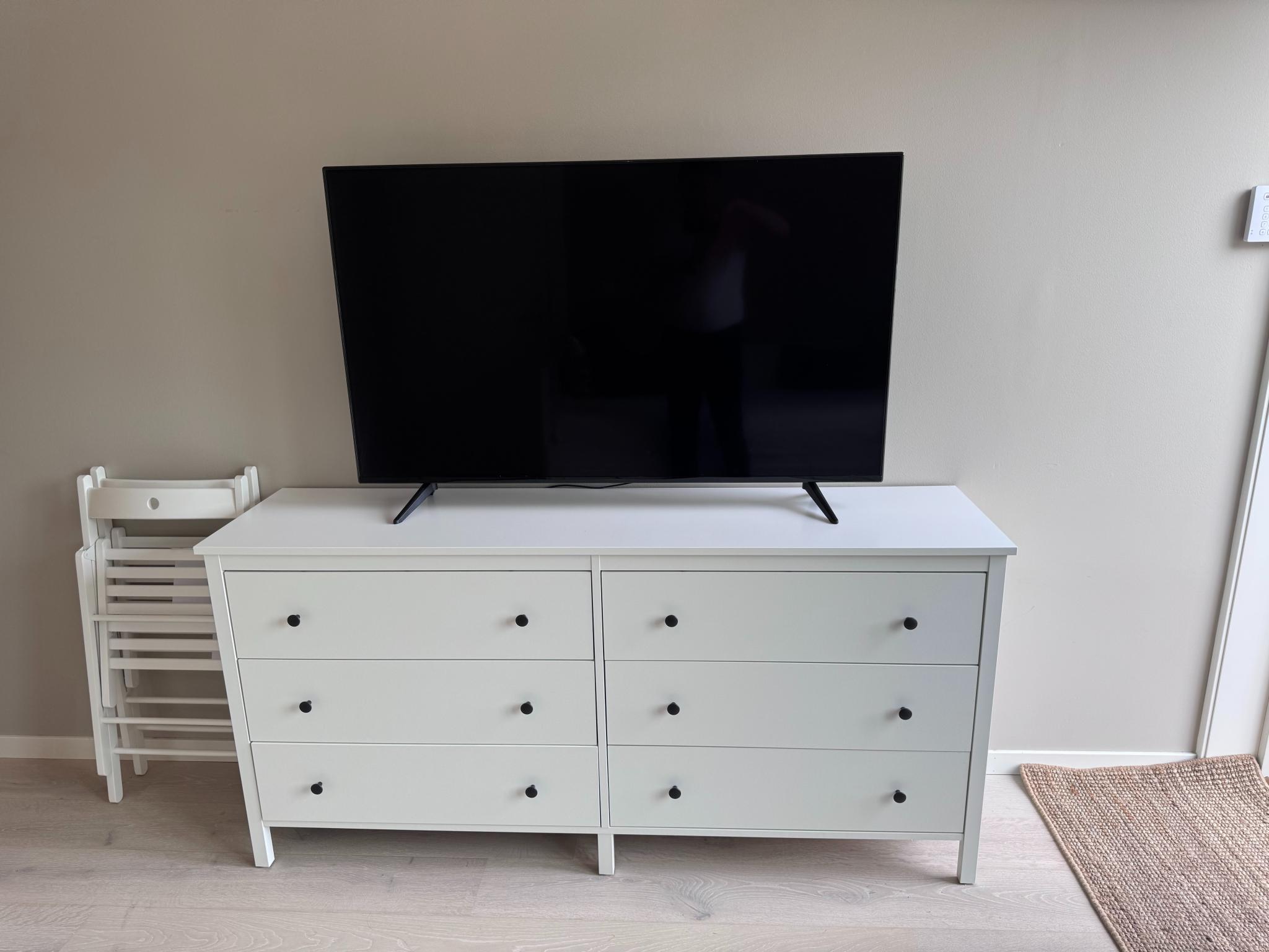 Romslig kommode, 65" TV og to stoler til kjøkkenbordet.