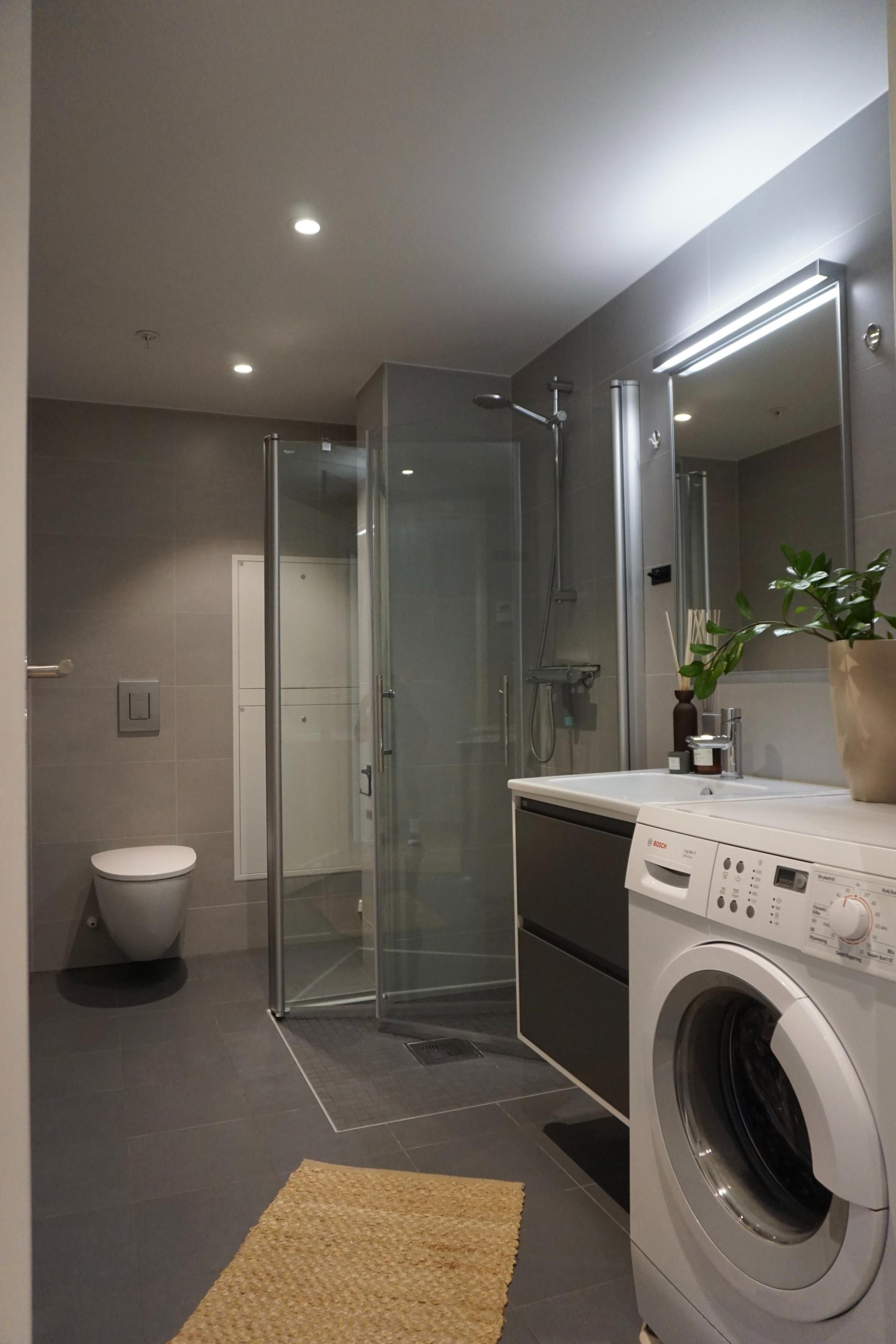Bad med dusjdører i glass og vaskemaskin