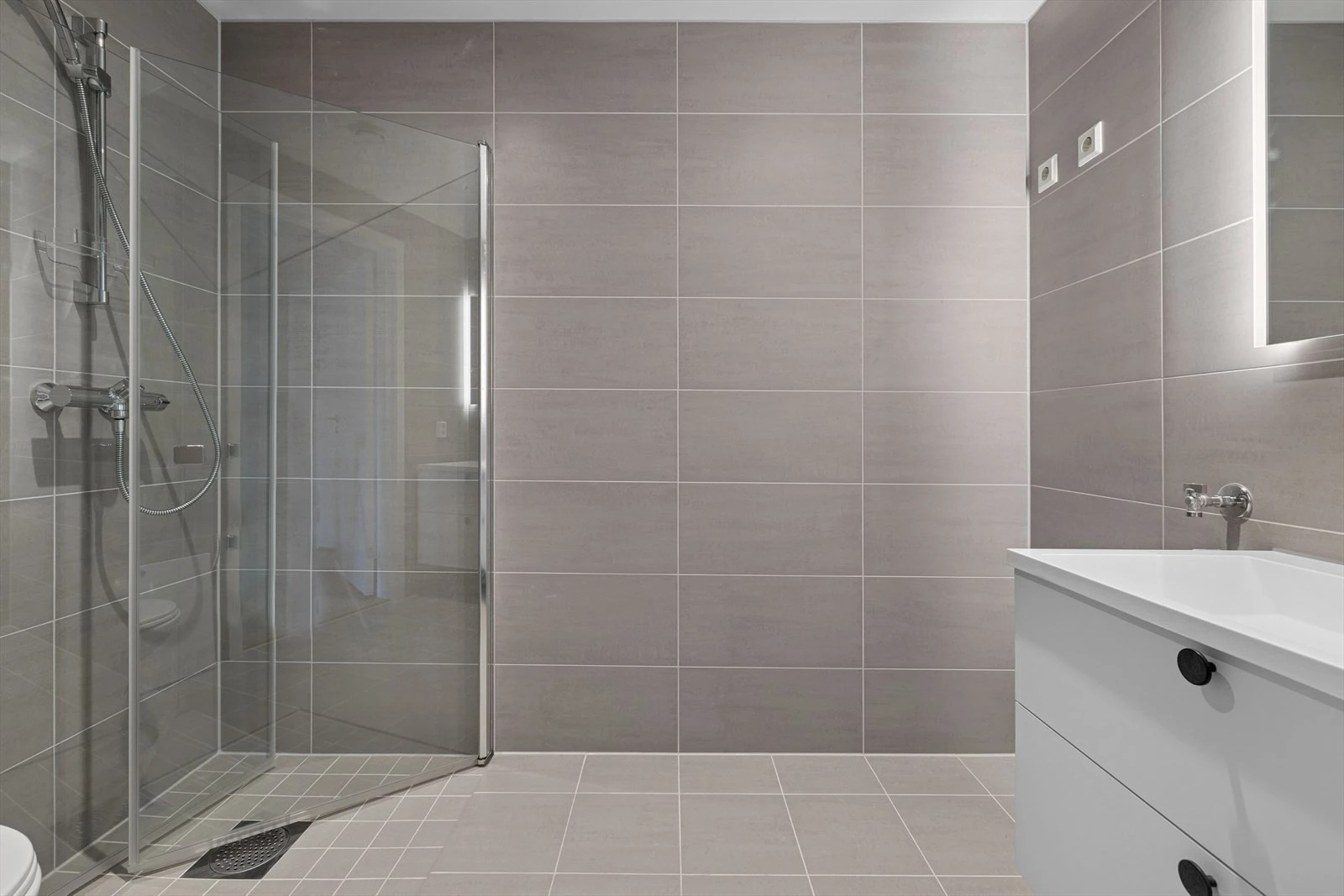 Delikat og moderne bad med fliser, dusjhjørne og opplegg for vaskemaskin.

