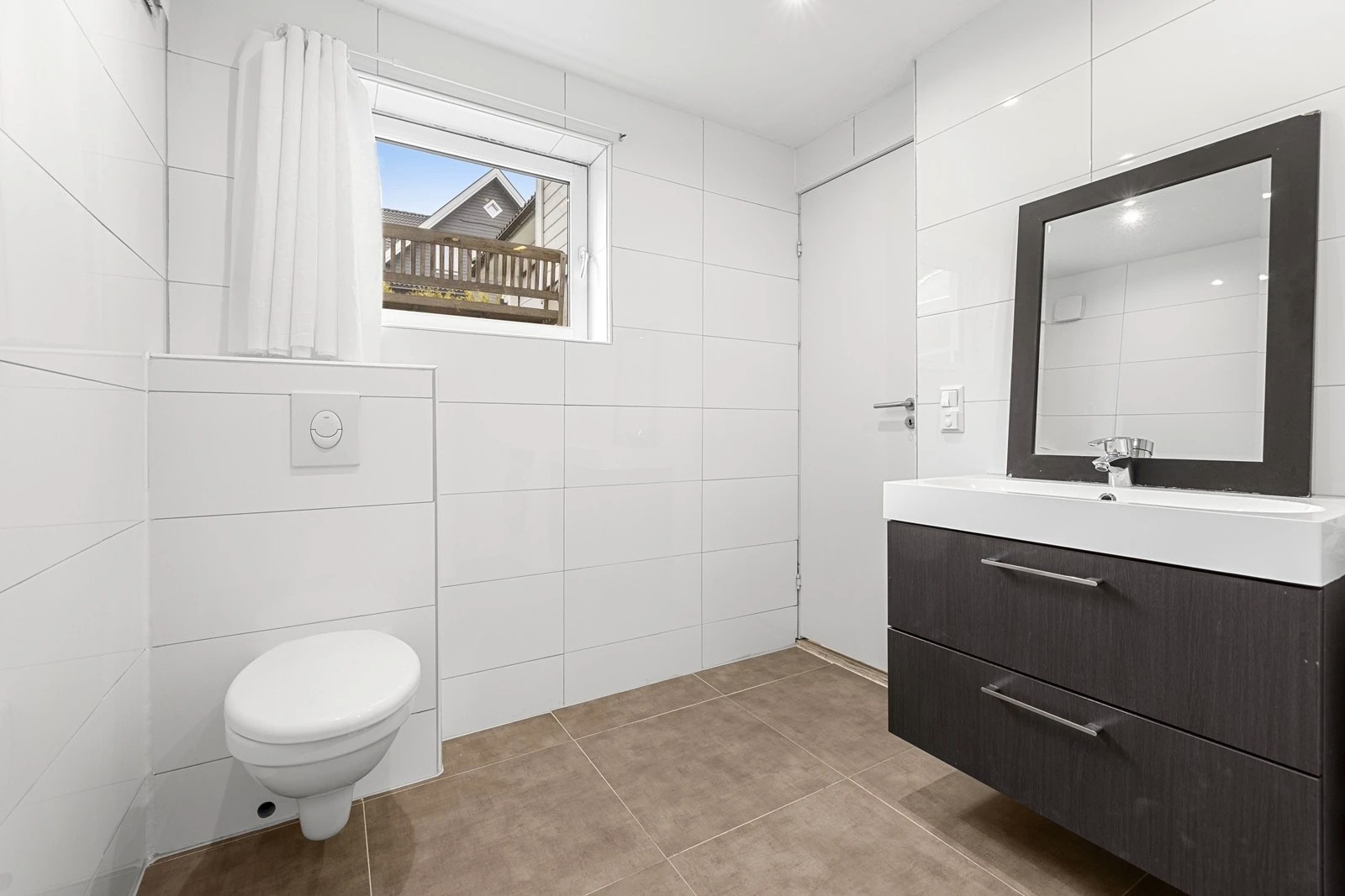 Baderommet er flislagt med vegghengt toalett, servant med skuffer og dusjnisje med forheng.