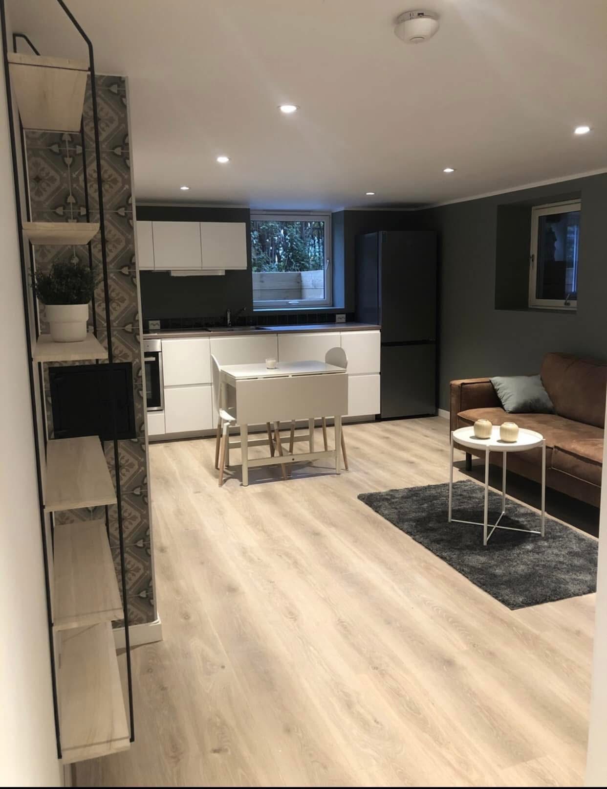 Kjøkken med hvitevarer og oppvaskmaskin. Stue med sofa og bord. 