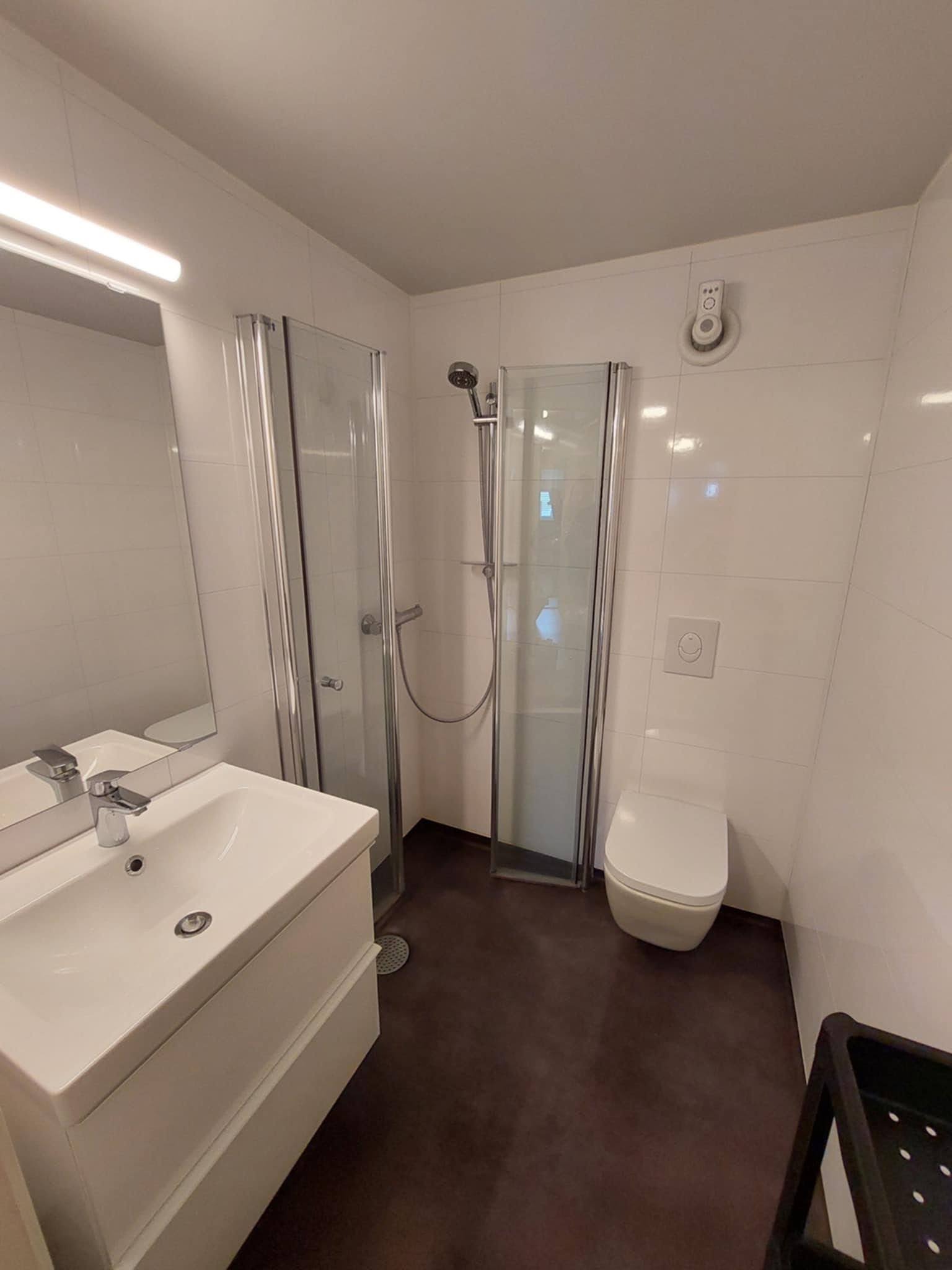 Bad med dusjhjørne, vegghengt toalett og vask.