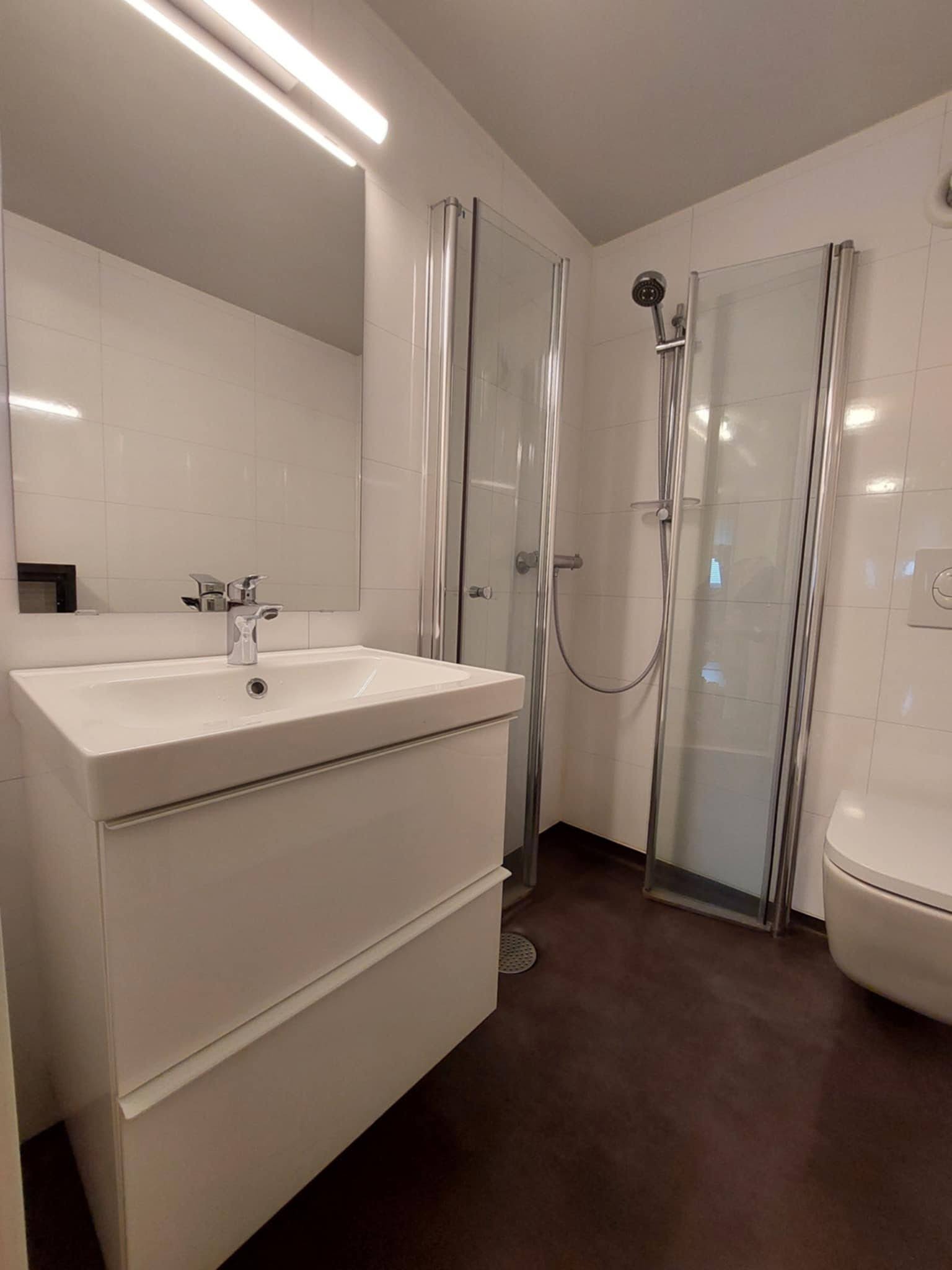 Bad med dusjhjørne, vegghengt toalett og vask.