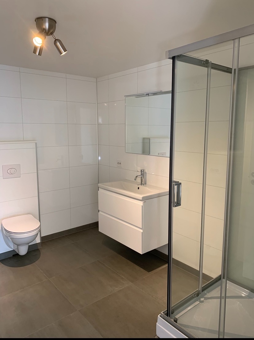 Bad med vegghengt toalett, dusjkabinett og opplegg for vaskemaskin og tørketrommel.