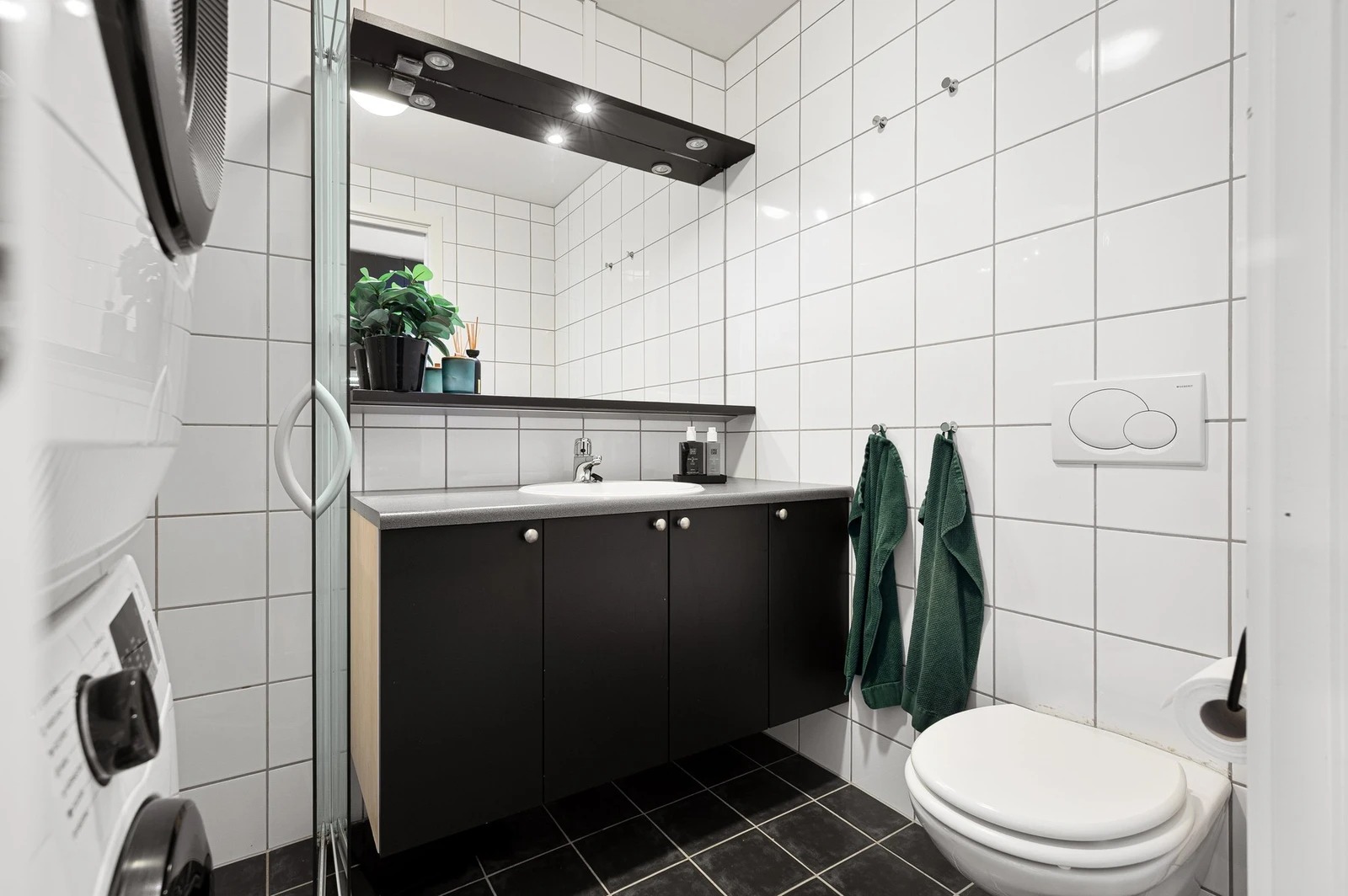 Badet er innredet med moderne servantløsning, speil med belysning og vegghengt toalett.