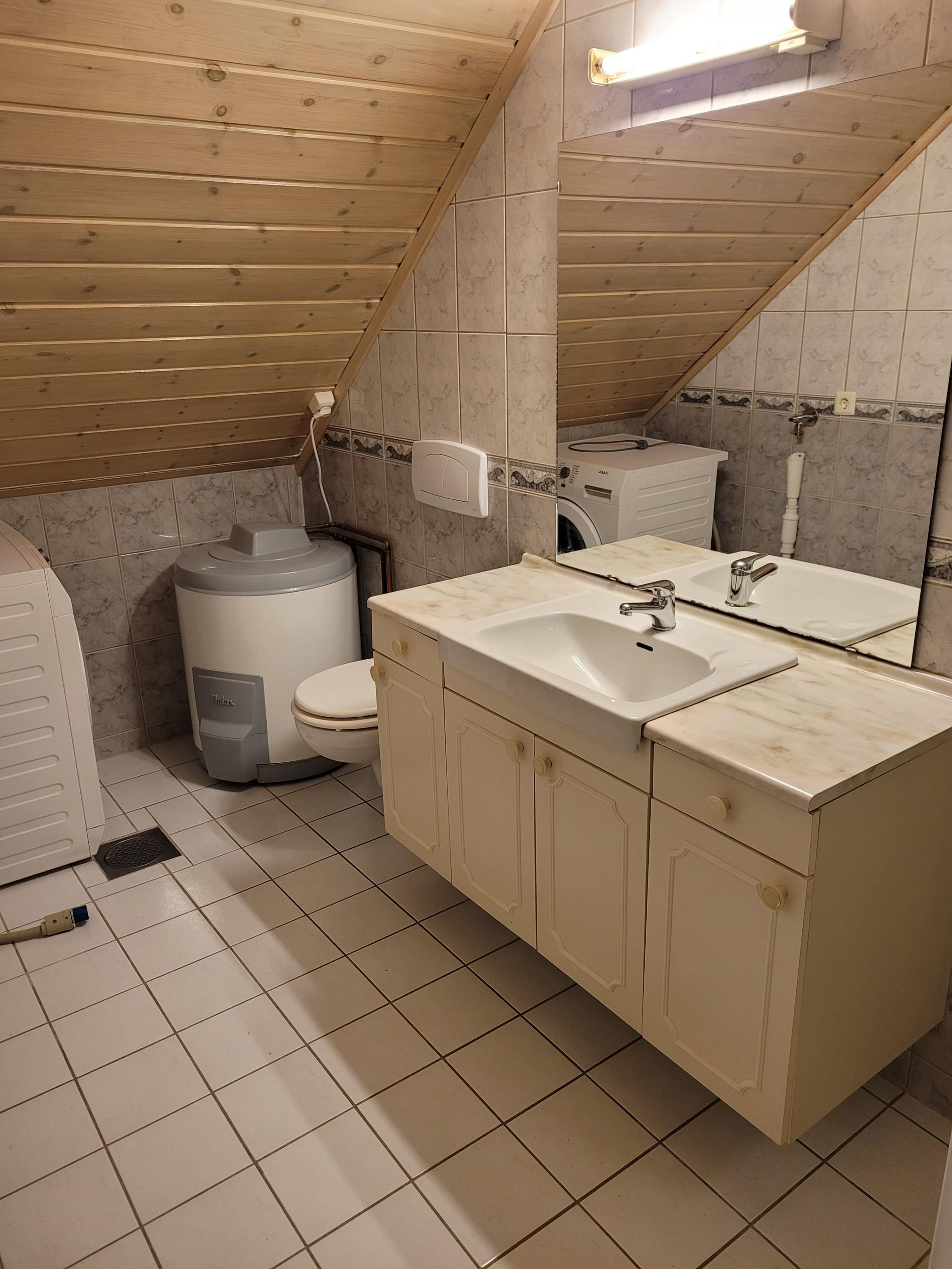 Bad med varmekabler i gulv, servantskap, speil, lys, vegghengt toalett, dusjhjørne, skap, varmtvannsbereder og opplegg for vaskemaskin. Vaskemaskina medfølger ikke.