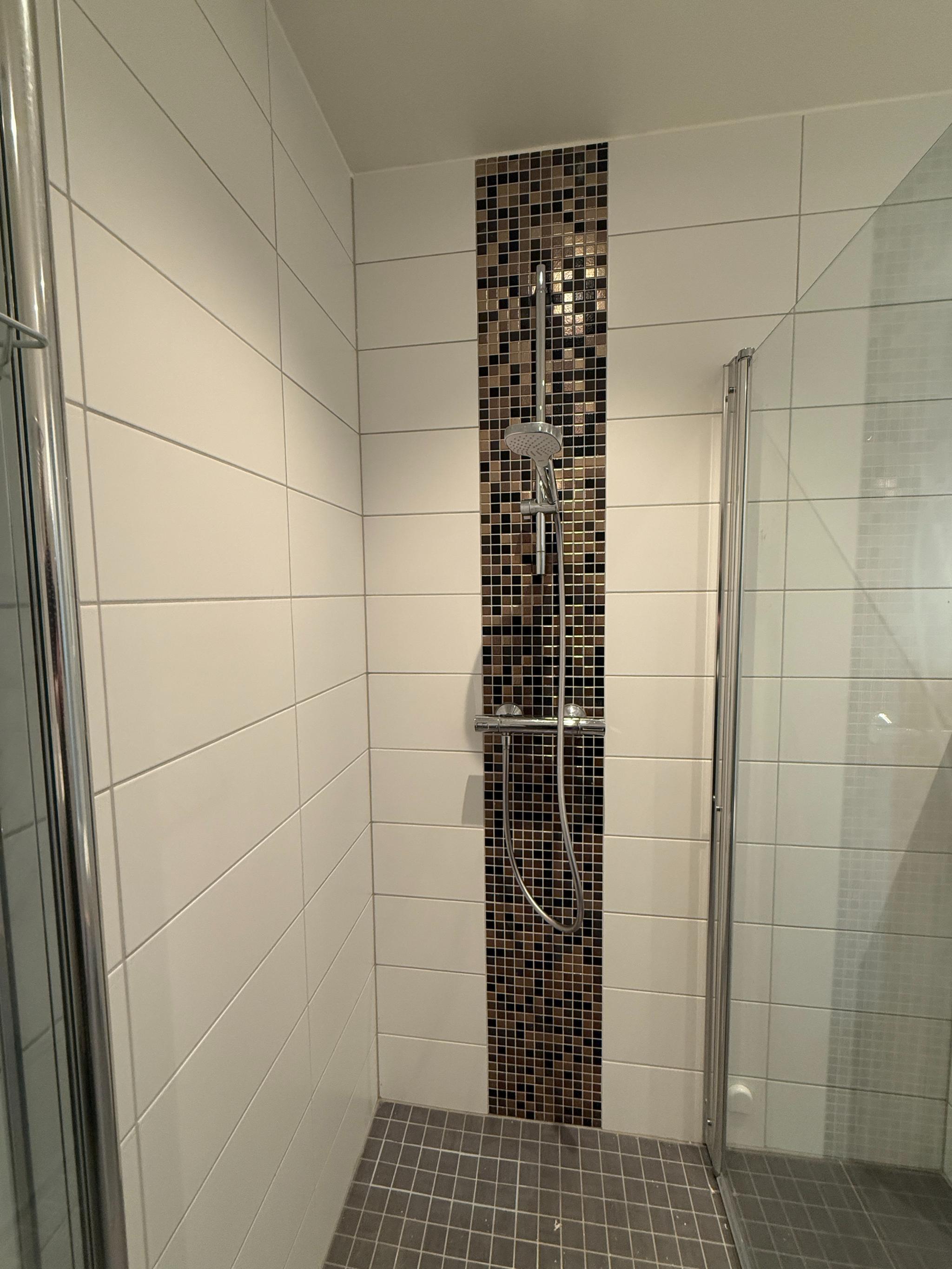 Delikat, flislagt bad med dusjhjørne på 90x90cm og moderne mosaikkdetaljer. Tidløst uttrykk og enkelt vedlikehold.