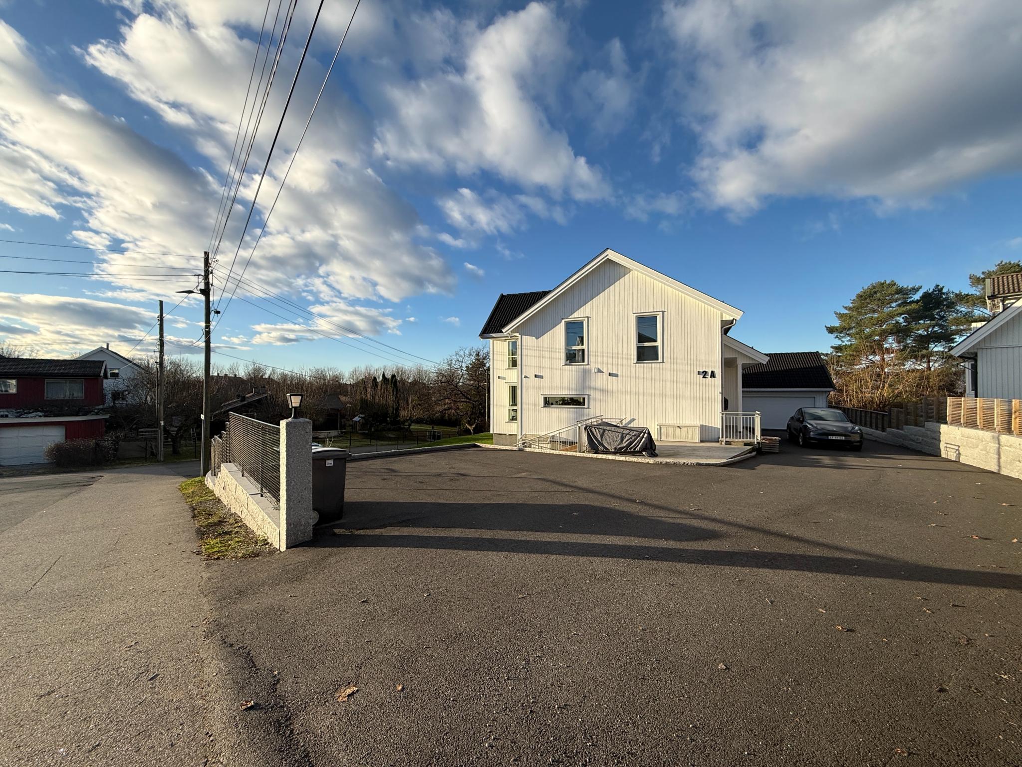 Inngangsparti og parkeringsplass foran boligen. Asfaltert område med god plass til parkering og enkel adkomst fra vei.