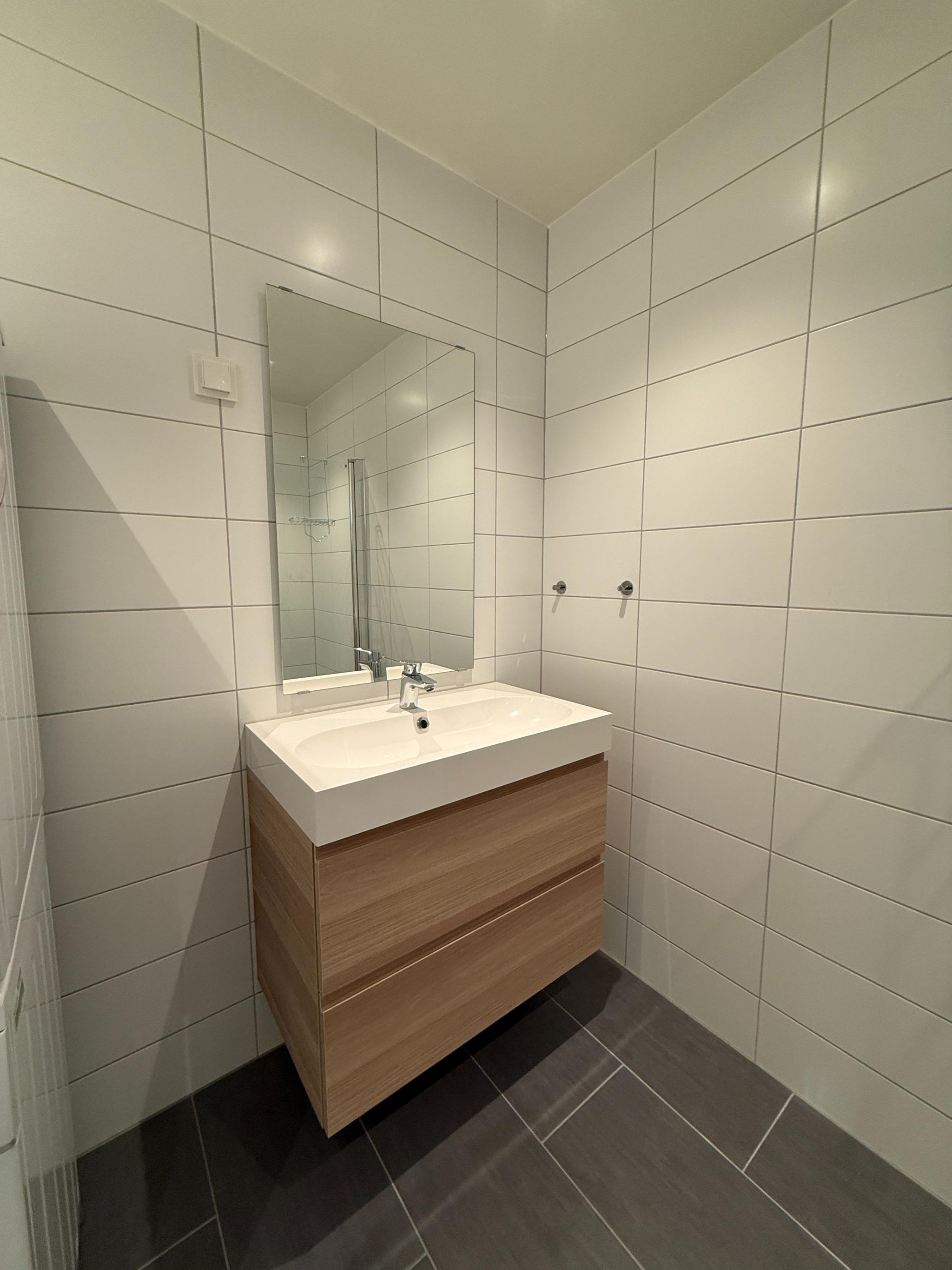 Stilrent bad med heldekkende fliser og moderne baderomsinnredning. Romslig servantskap med store skuffer, speil og spotbelysning.