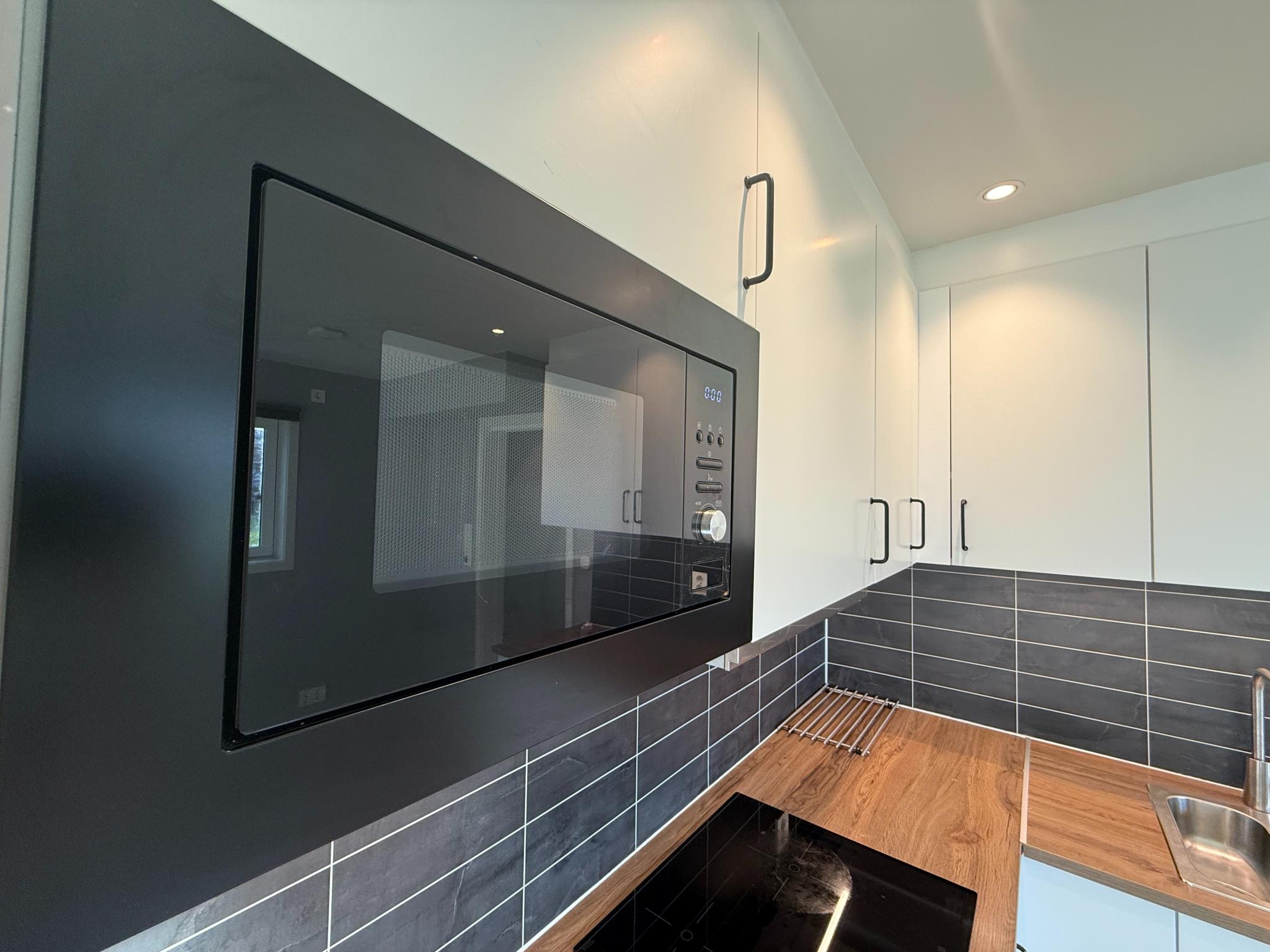 Moderne kjøkken med integrert mikrobølgeovn og god skapplass. Flislagt sprutplate og innfelte spotter gir et lyst og funksjonelt uttrykk.