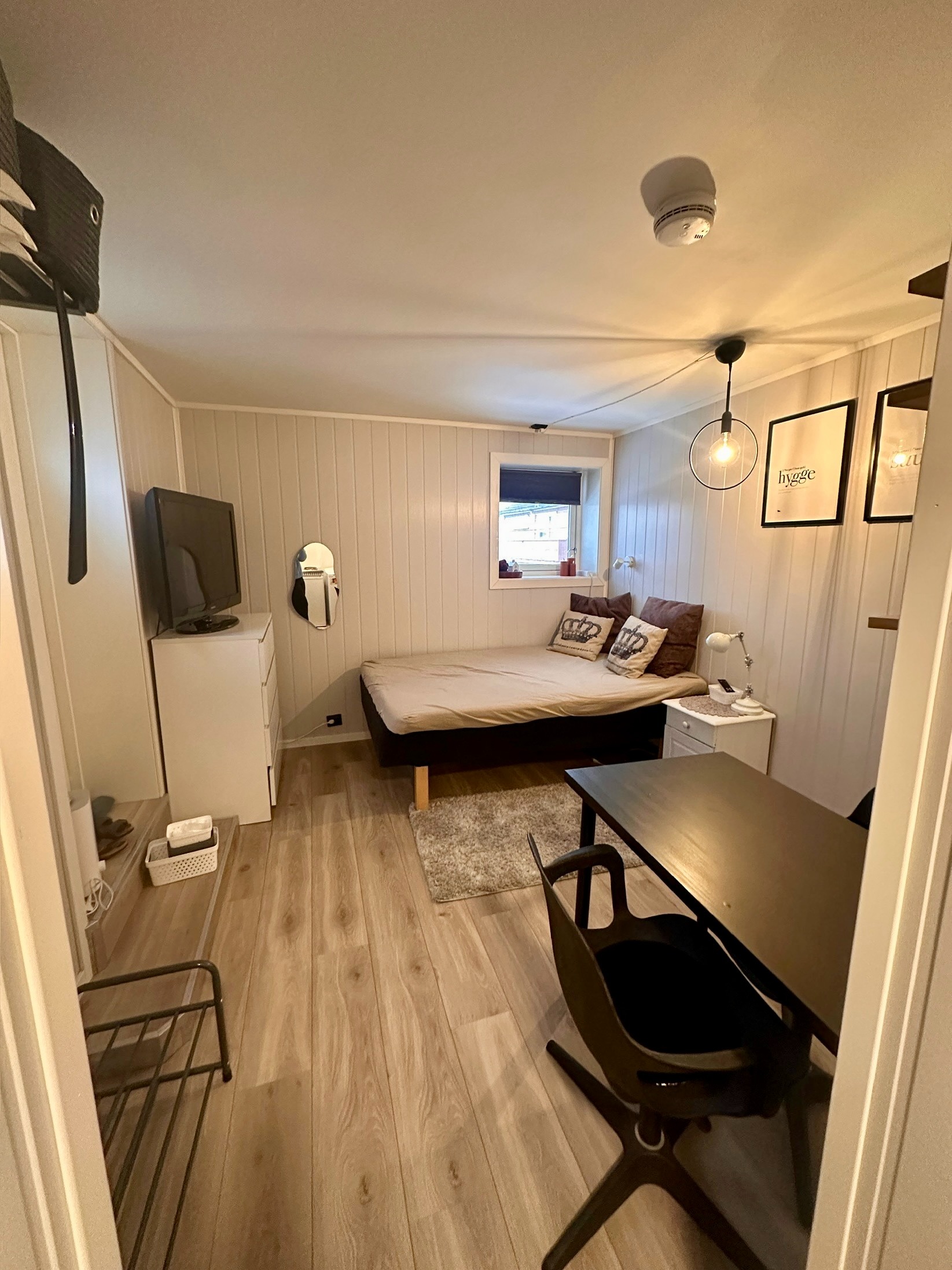 Praktisk møblert hybel med vindu, skrive-/spiseplass og rolig atmosfære.