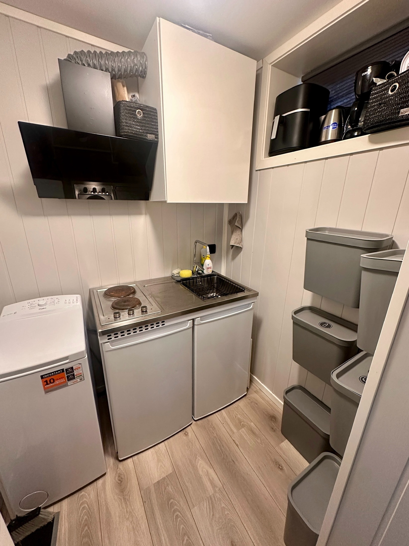 Kompakt kjøkkenkrok med kokeplater, vask, kjøleskap, oppbevaring og egen liten vaskemaskin.