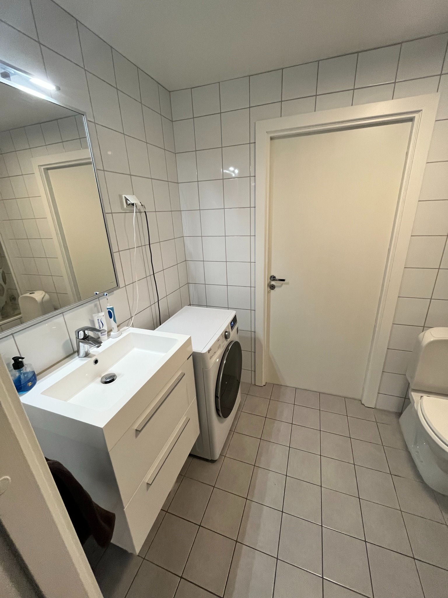 Pent flislagt baderom med moderne servantmøbel og praktisk vaskemaskin.