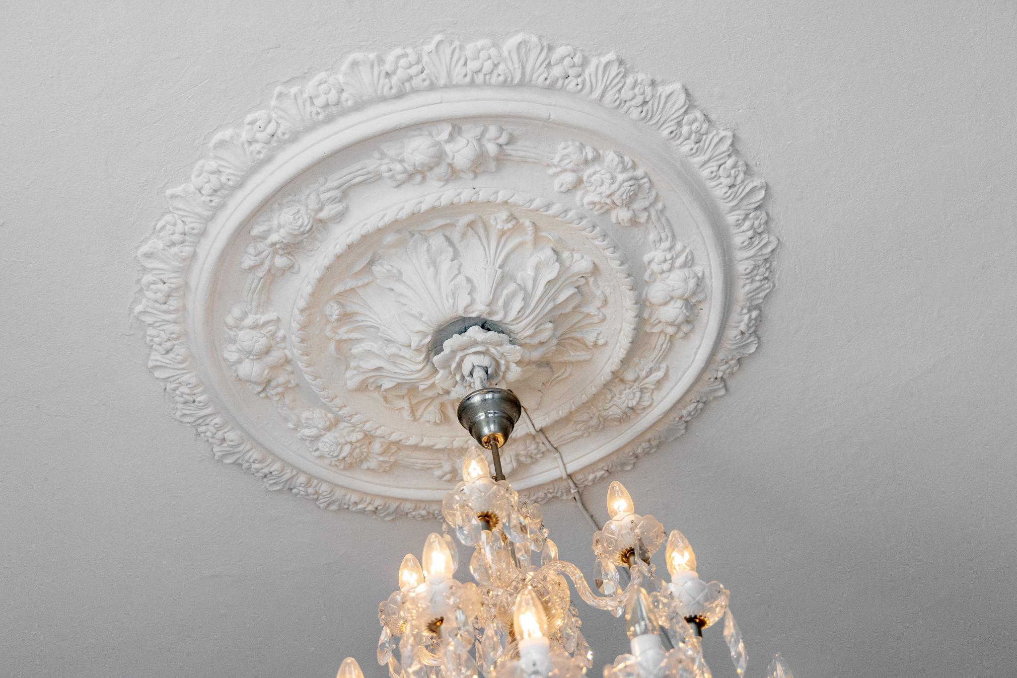 Klassiske detaljer som rosett og krystall lysekrone i stuen, med i alt 16 lys. Kan dimmes.