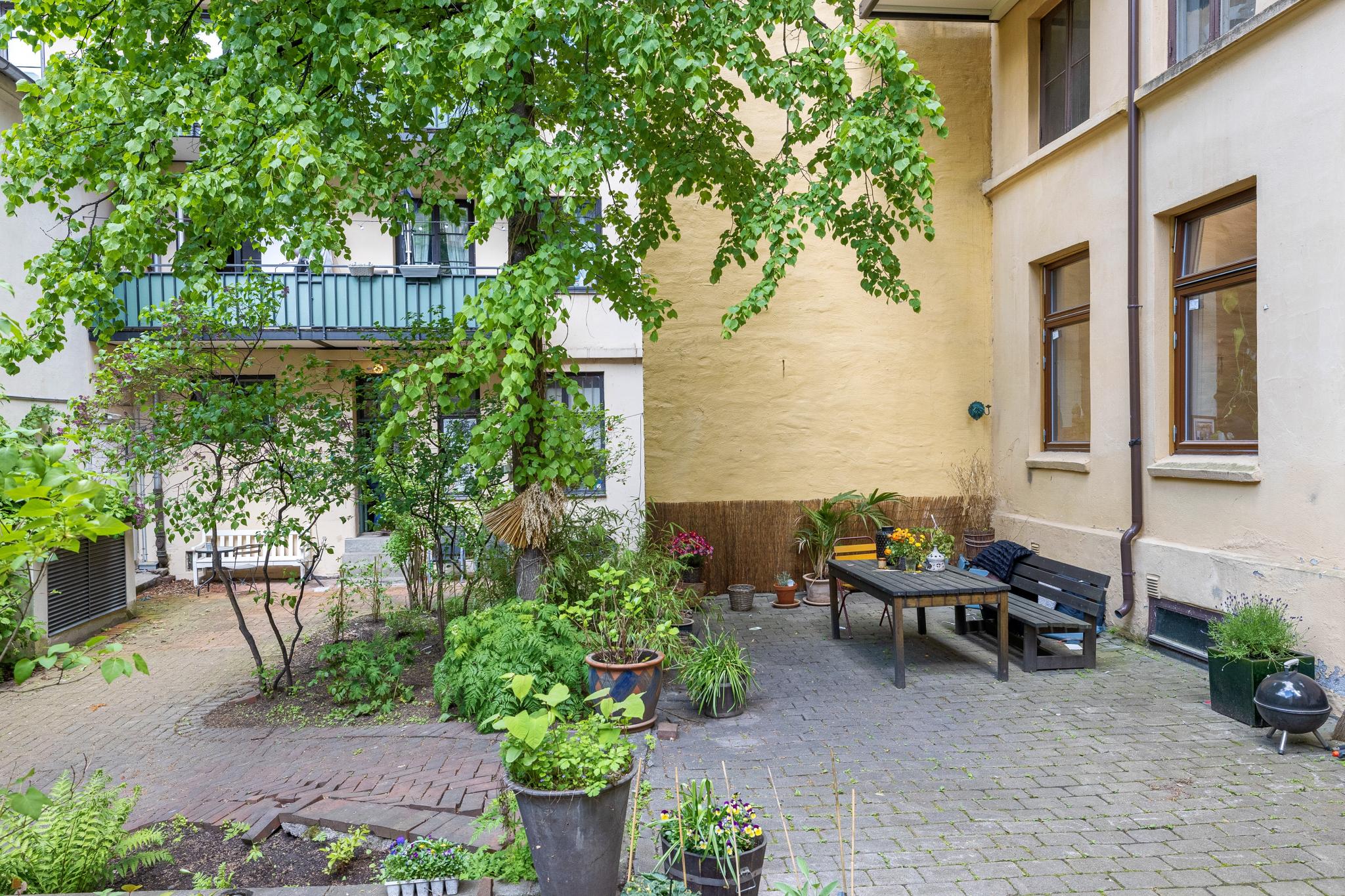 Koselig felles bakhage med blomsterpotter og prydplanter. Felles sittegruppe som kan brukes av alle som bor i gården.