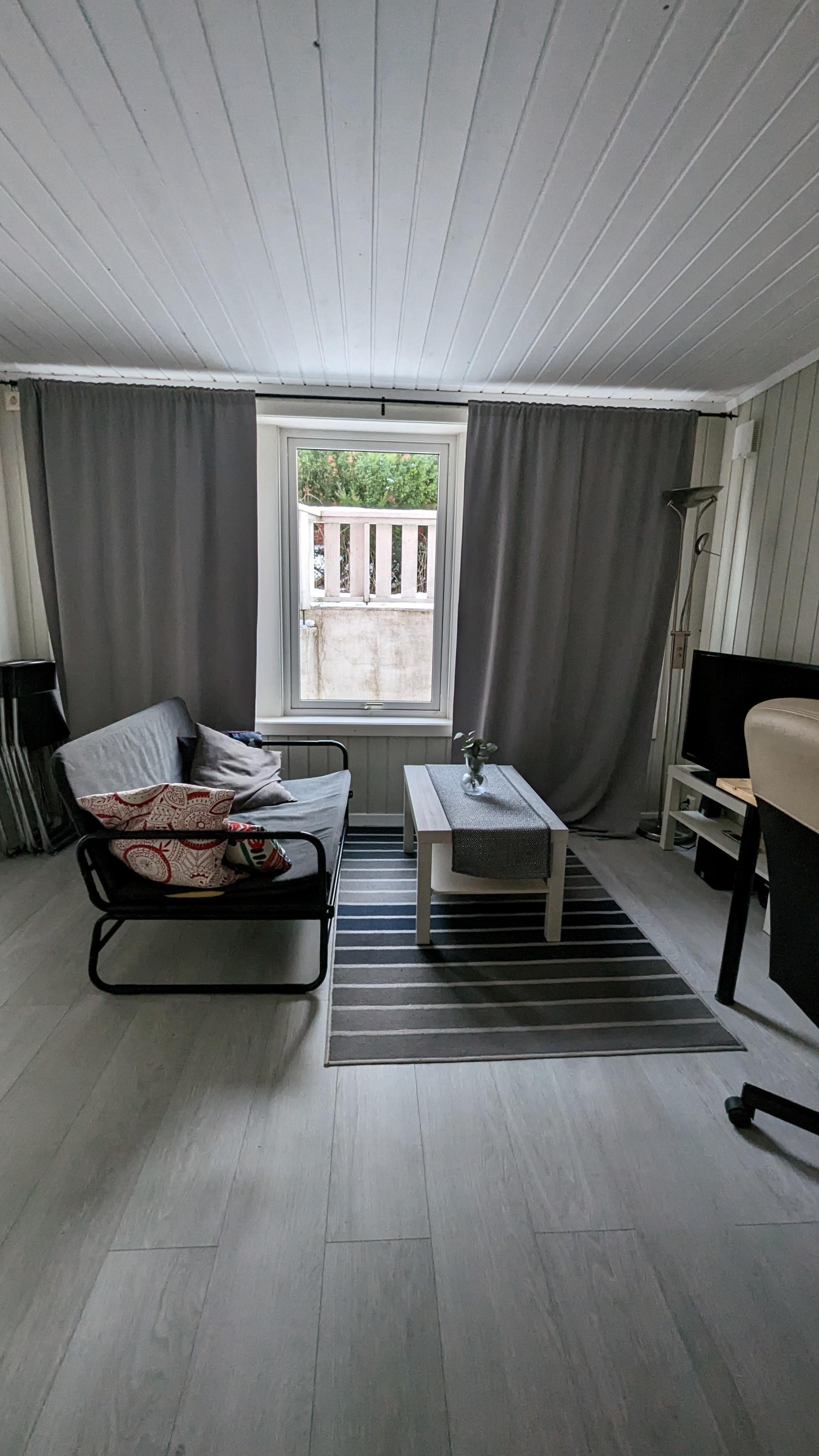 stue. det er god plass til spise bord og arbeidsbord. store vindu hele veggen( på bildet dekket med gardiner.