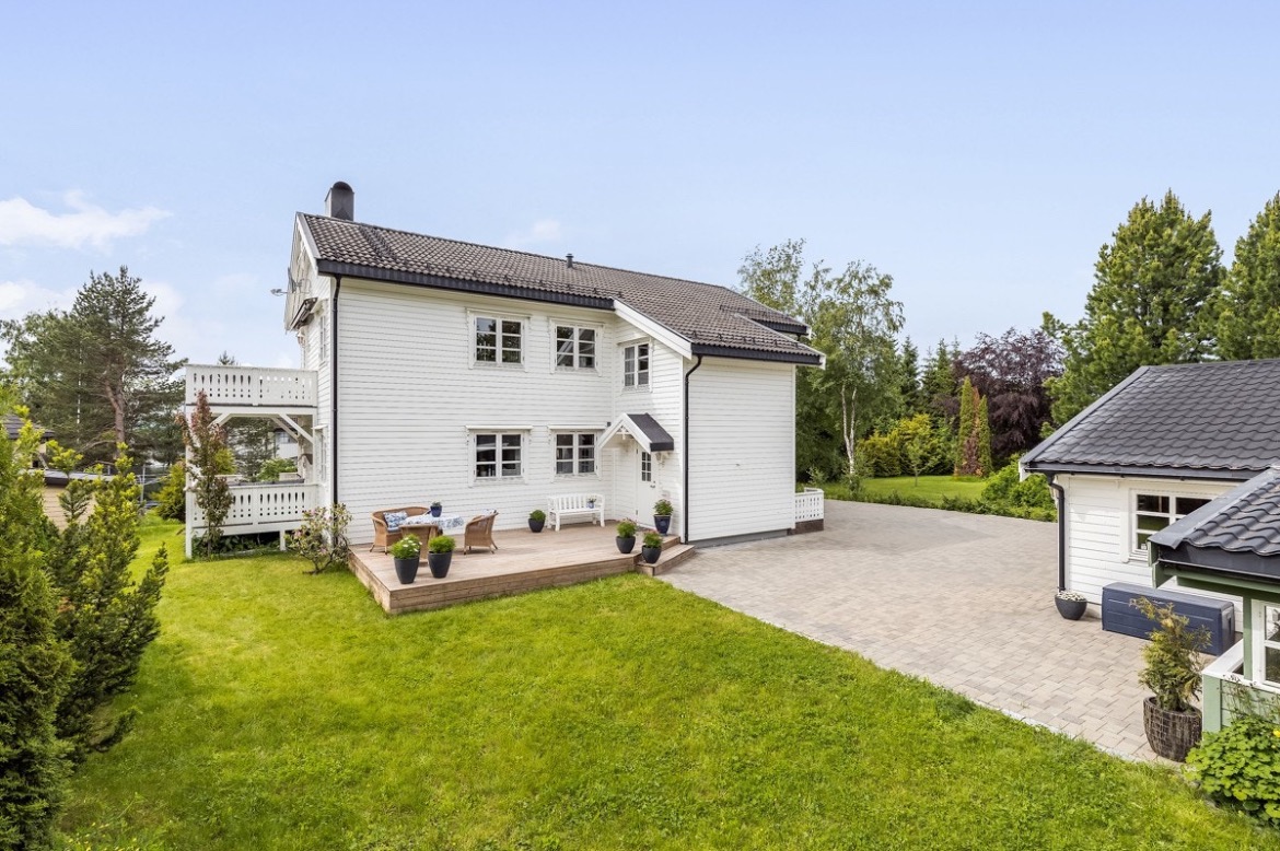 Her er bilde fra plenen som hører til og da ser man sin private balkong oppe til ventre, privat markterrasse med egen inngan som har takoverbygg. Parkering og starten på uteboden til høyre