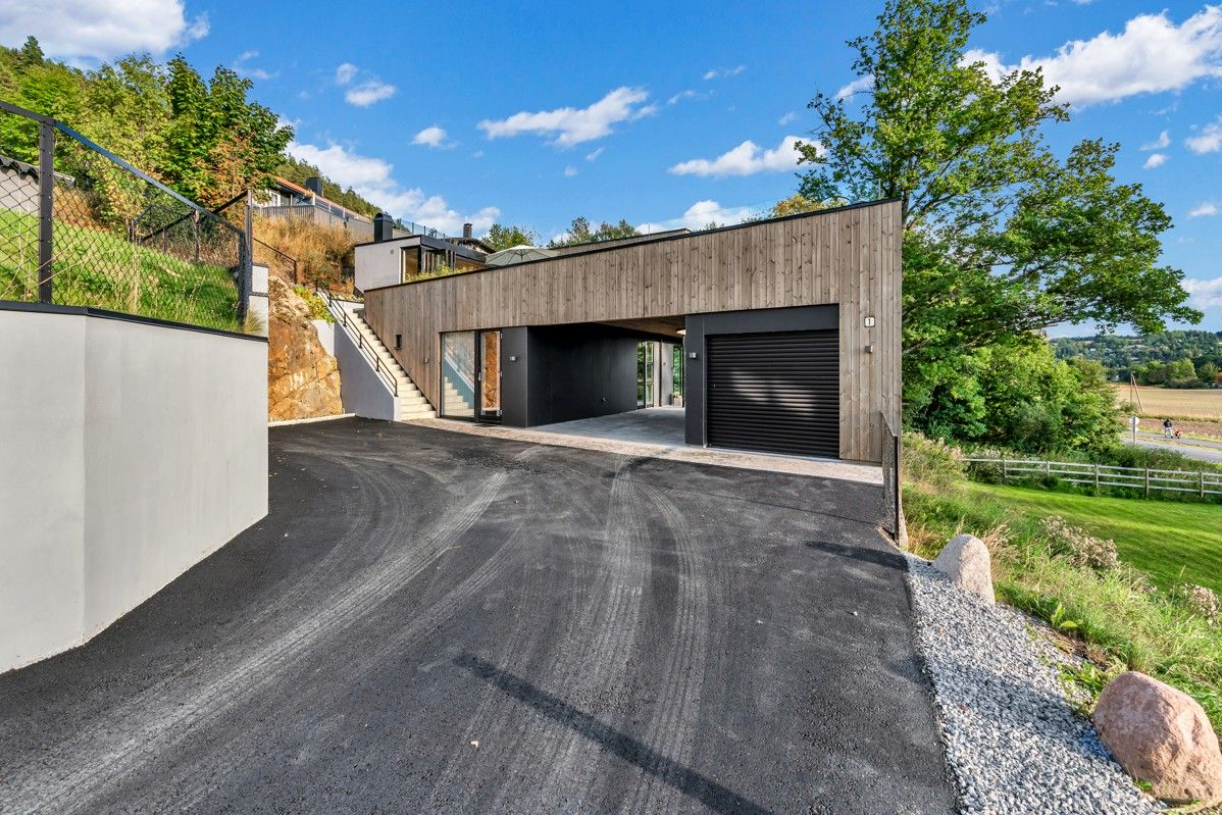 Inngangsparti med vindu og inngangsdør ses mellom trapp ned fra terrassen til venstre og carport 