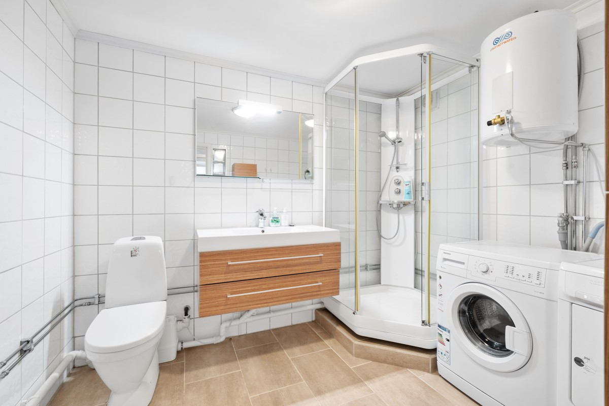 Bad med dusjkabinett, vaskemaskin og tørketrommel.