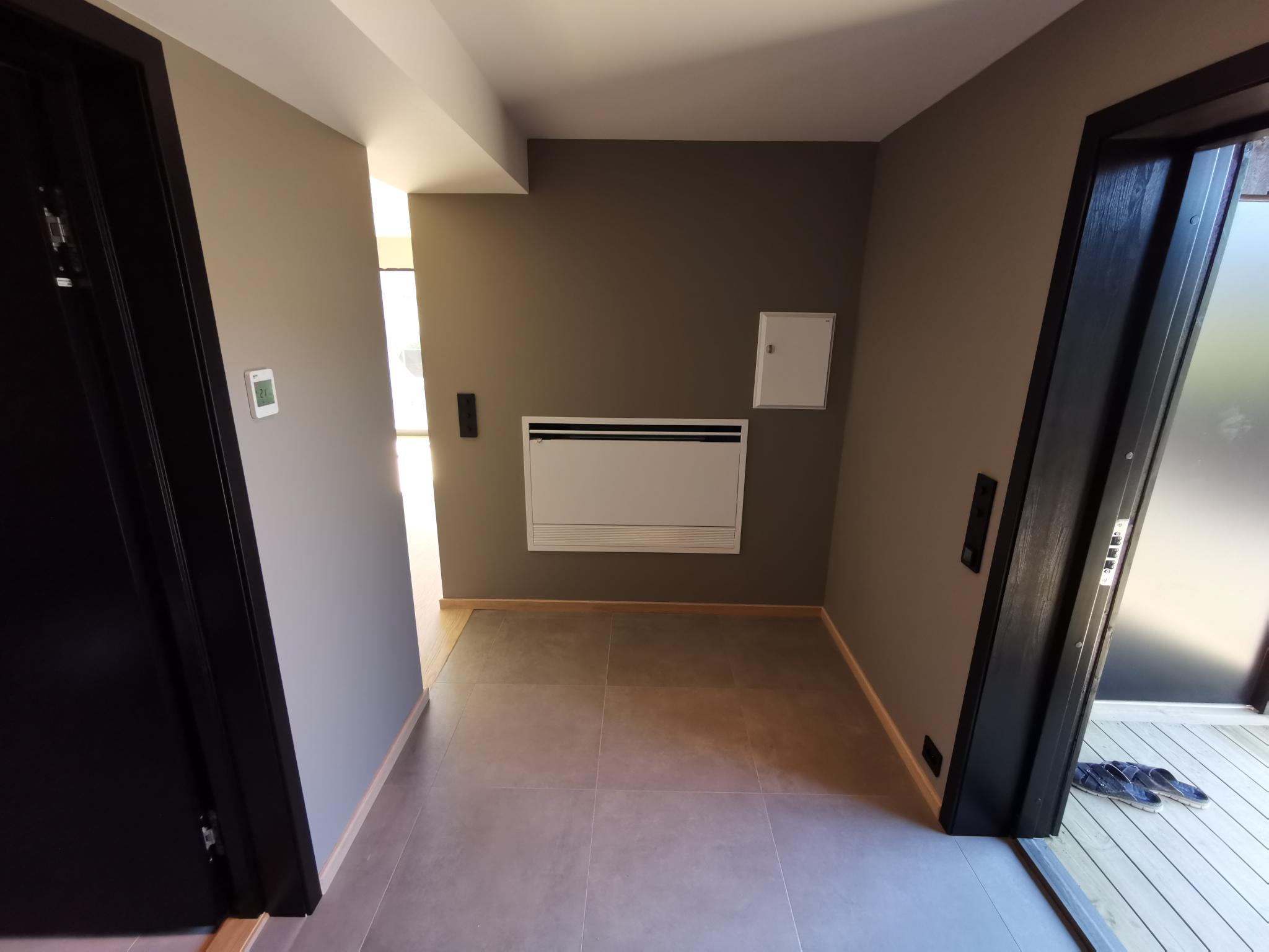 Entre med bad til venstre og inngangsdør til høyre. Viftekonvektor for kjøling via bergvarmeanlegg på veggen rett frem.