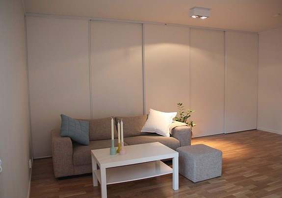 Stue har lyse forhold med 5 kvm stor skyvedørsgarderobe/ lagringsløsning bak sofa.