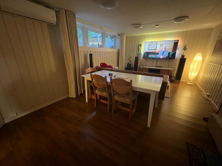 Stort kjøkkenbord med stoler og strømuttak så du kan se på TV og spise mat. Oppe i hjørnet ser man og varmepumpen