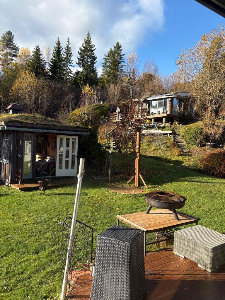 En del av hagen med grillhus og hytte oppi fjellet